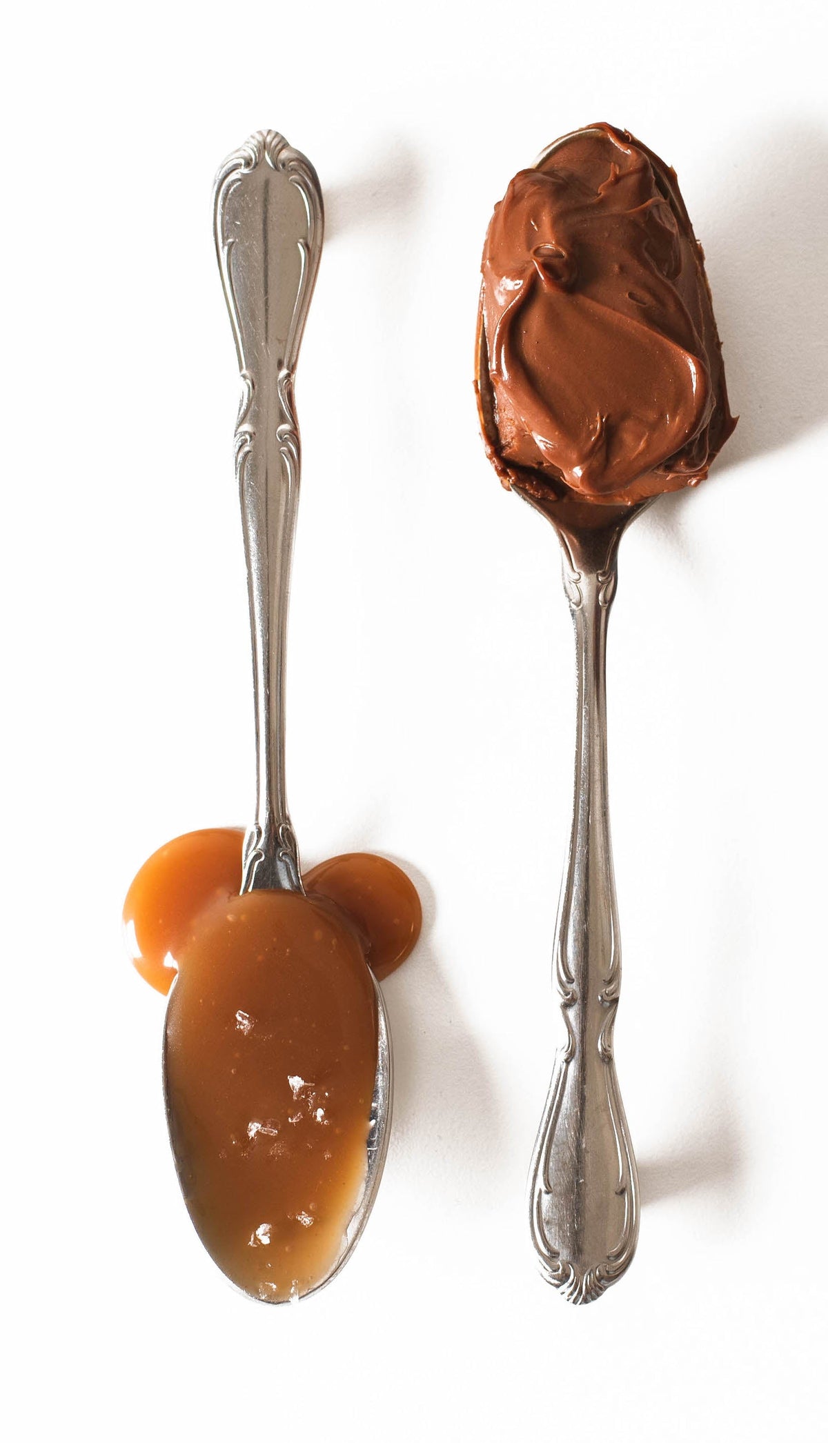 Two silver teapoons on a white background, one holds a thick chocolate dessert, the other a rich looking caramel sauce