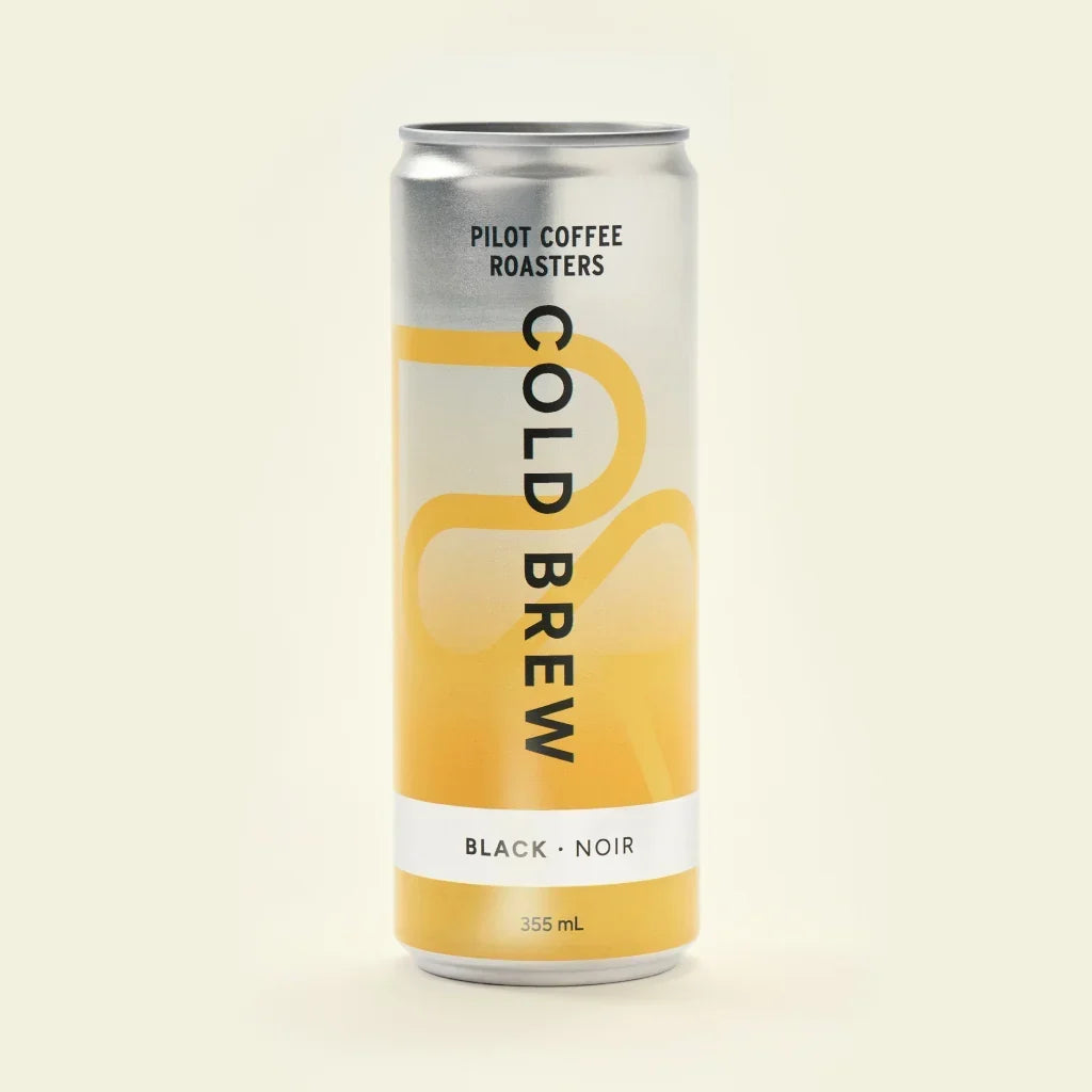 A straightforward product shot of a single 355-milliliter can of Pilot Coffee Roasters Black Cold Brew against a seamless light beige background. The can's design features a silver top fading into a yellow bottom with abstract curved lines.